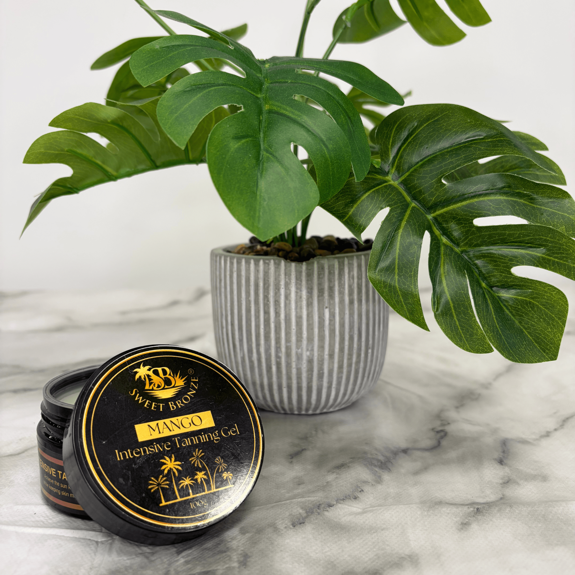 Mango Intensive Tanning Gel container on a marble surface with a plant in the background