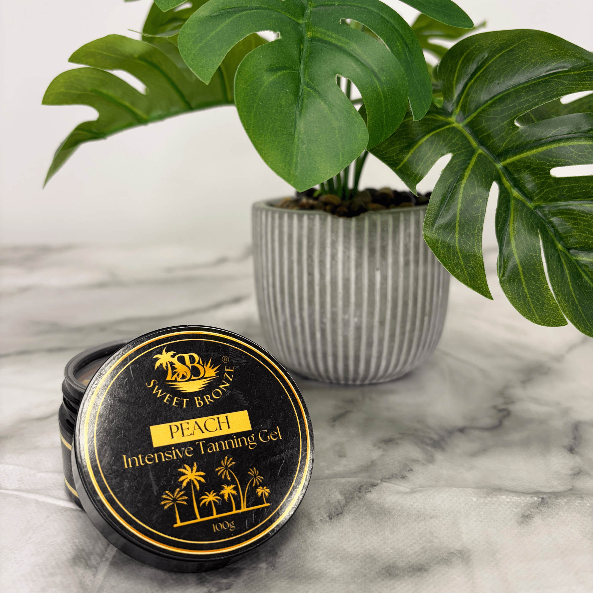 Jar of Sweet Bronze Peach Intensive Tanning Gel on a marble surface with a potted plant in the background