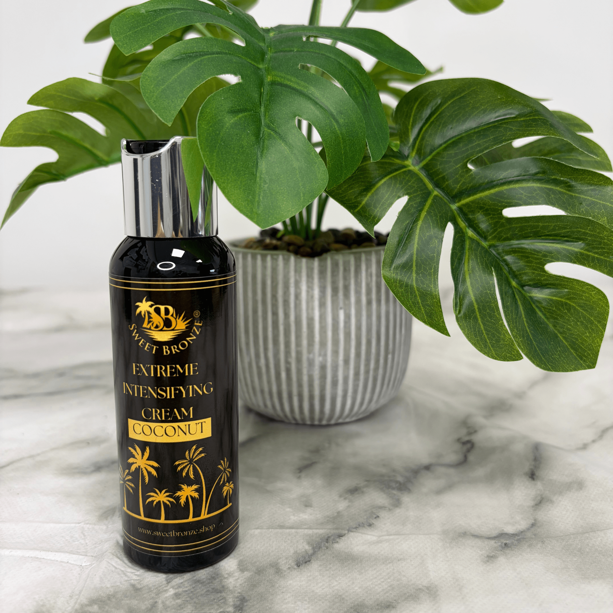Black bottle of 'Extreme Intensifying Cream Coconut' on a marble surface with a plant in the background