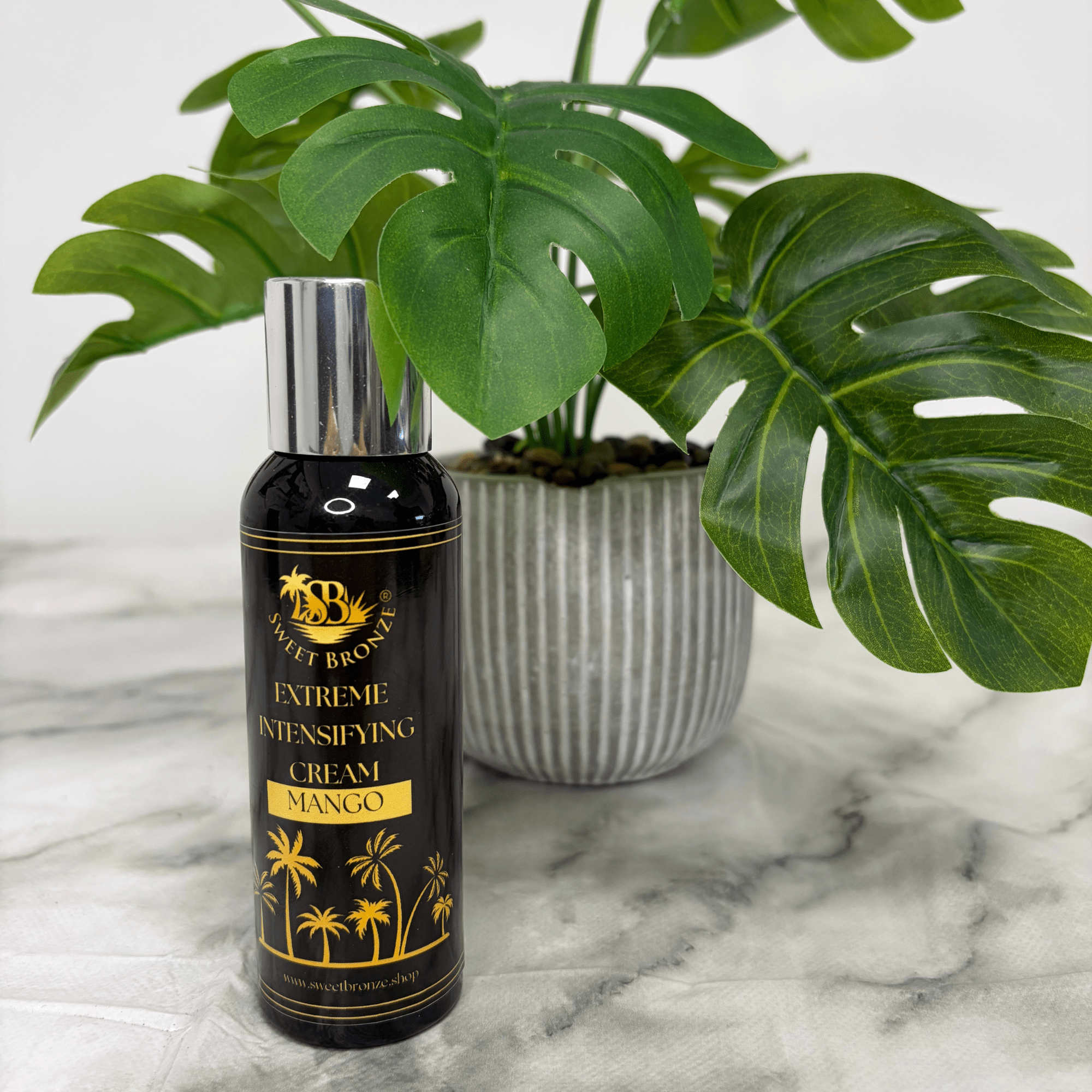 Mango Extreme Intensifying tanning cream on a marble surface with a plant in the background.