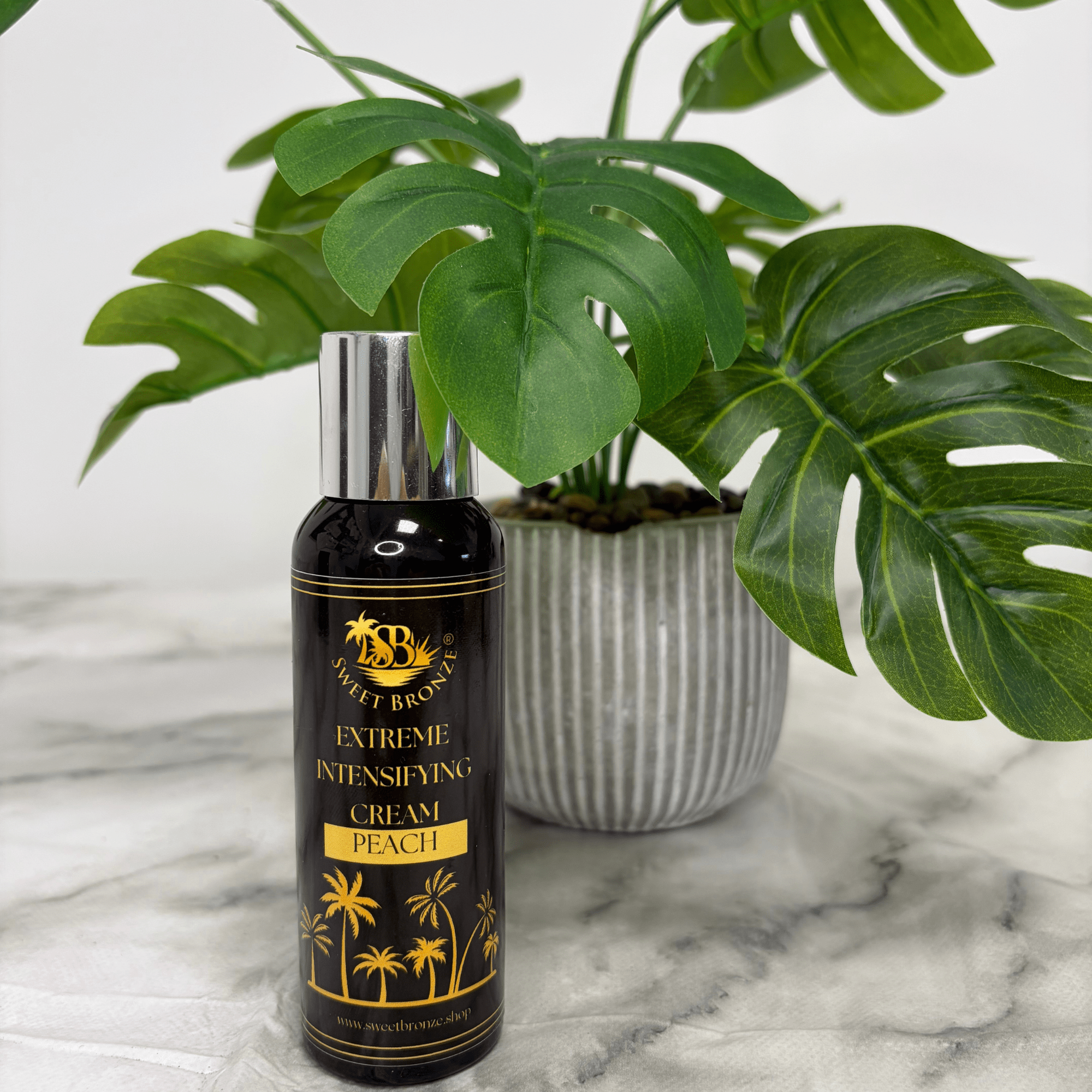 Black and gold bottle of 'Extreme Intensifying Cream Peach' with a plant in the background on a marble surface