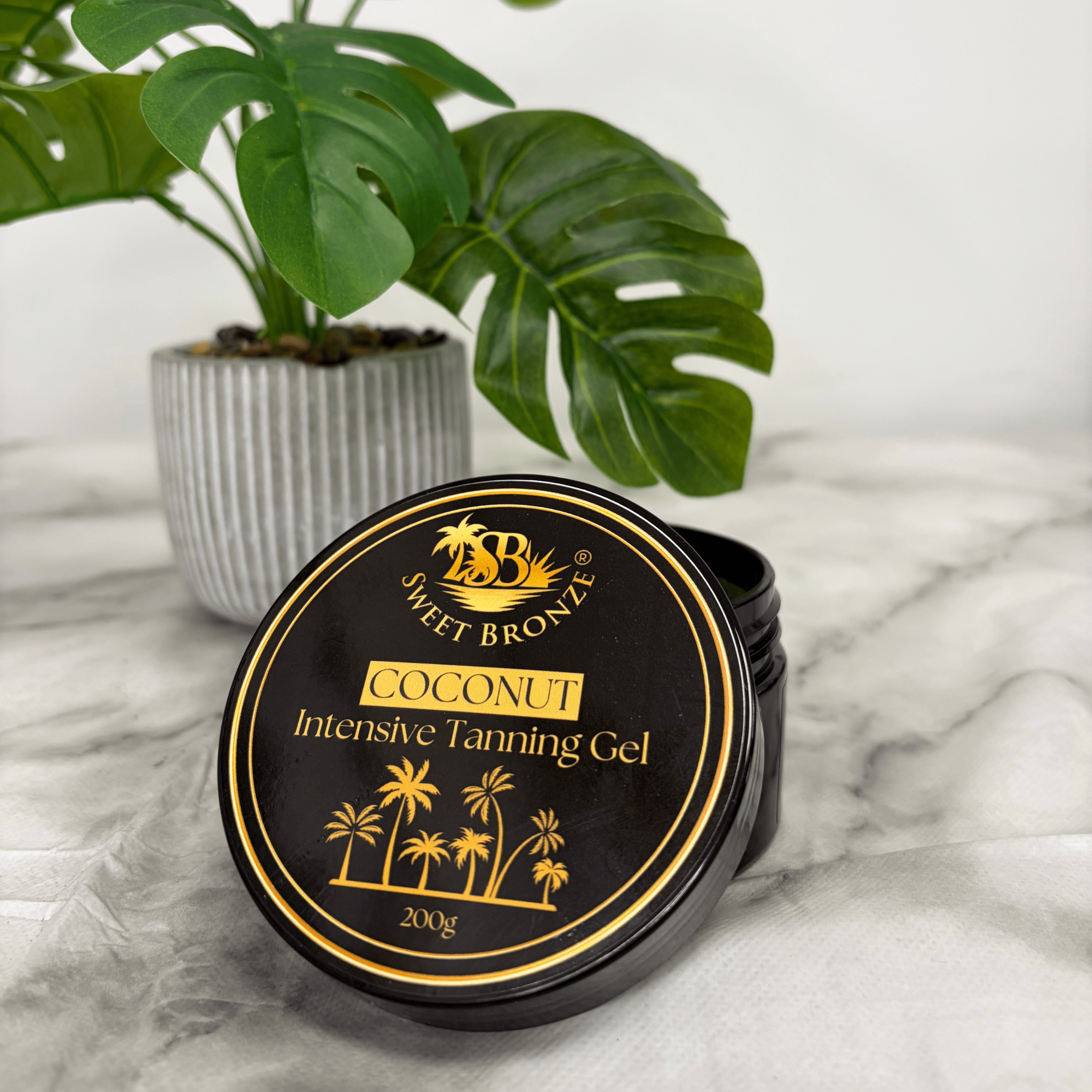 Sweet Bronze Coconut Intensive Tanning Gel container on a marble surface with a plant in the background
