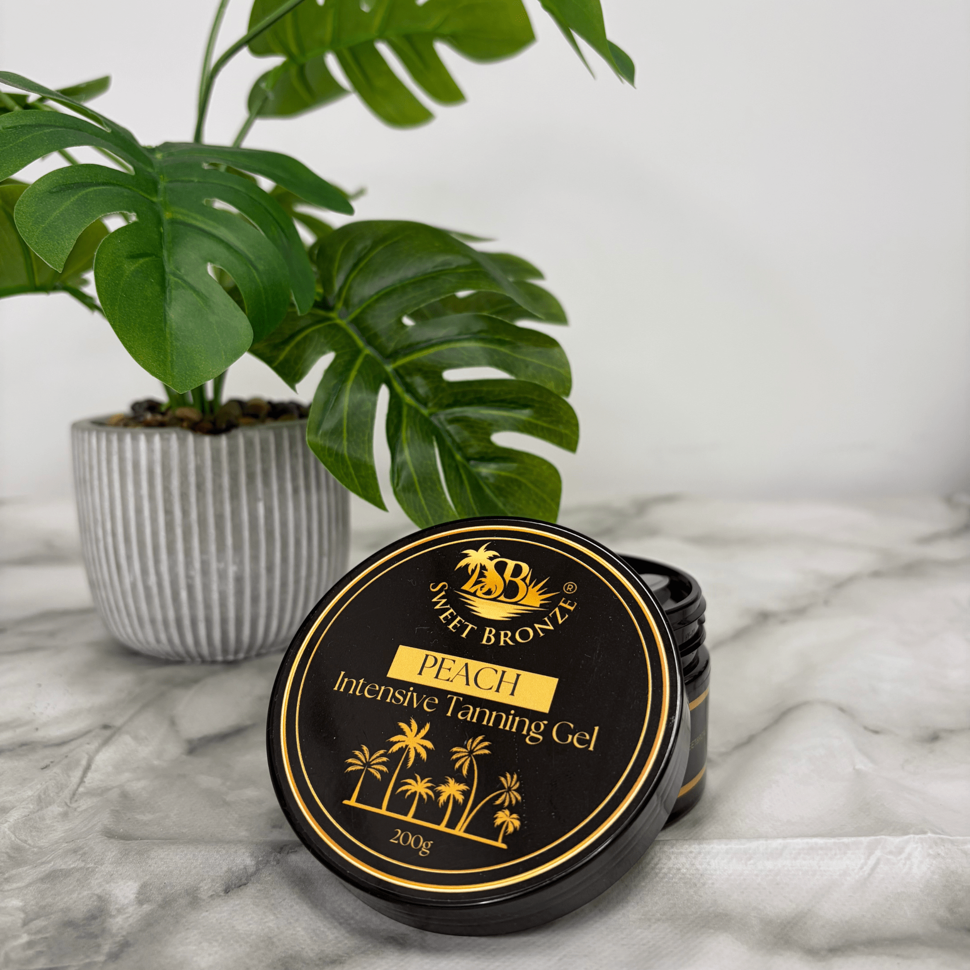 Sweet Bronzo Peach Intensive Tanning Gel container on a marble surface with a plant in the background