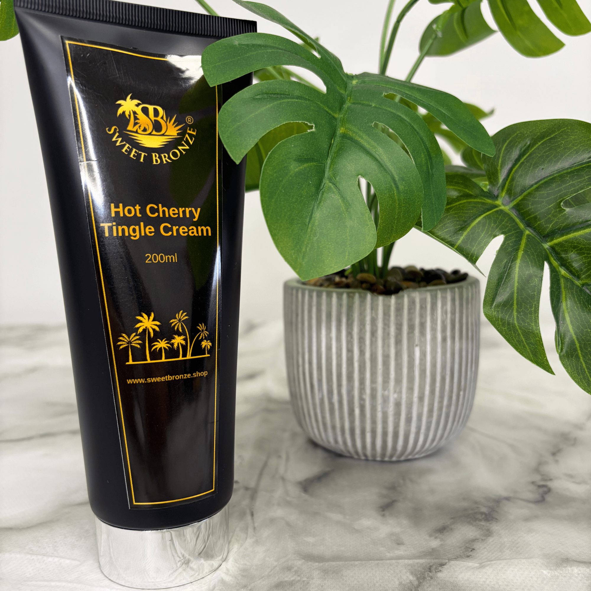 Black tube of Sweet Bronze Hot Cherry Tingle Cream with a plant in the background