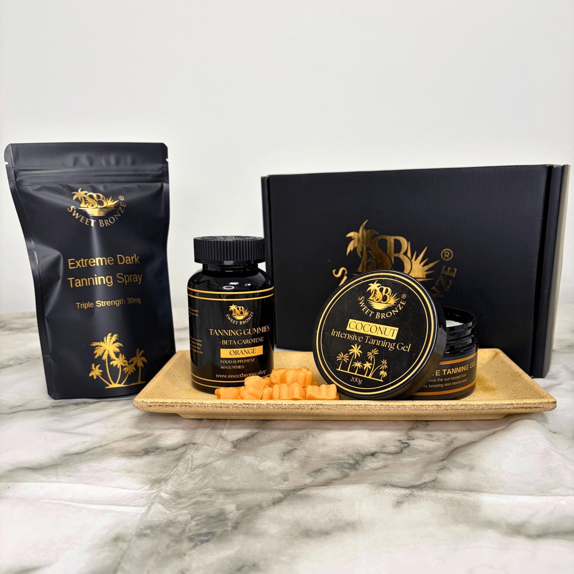 Collection of tanning products including spray, gel, and cream on a marble surface with a branded box.