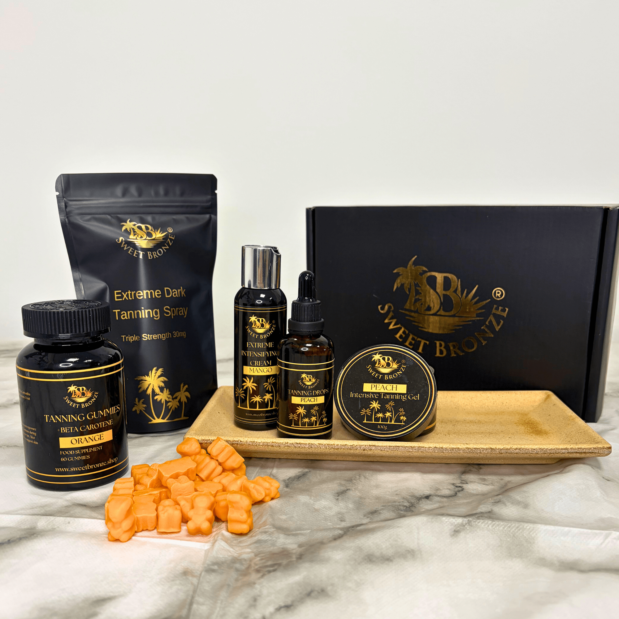 Collection of Sweet Bronze tanning products on a marble surface with a white background