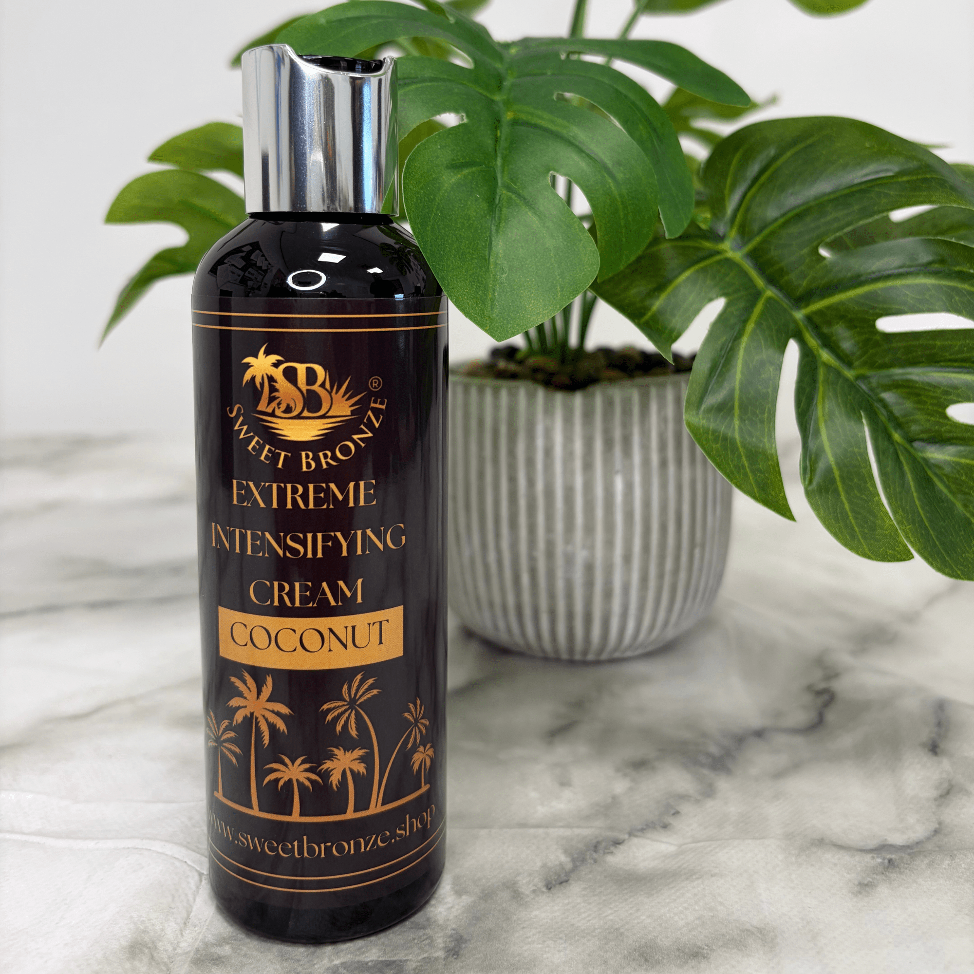 Bottle of Sweet Bronze Extreme Intensifying Cream Coconut on a marble surface with a plant in the background