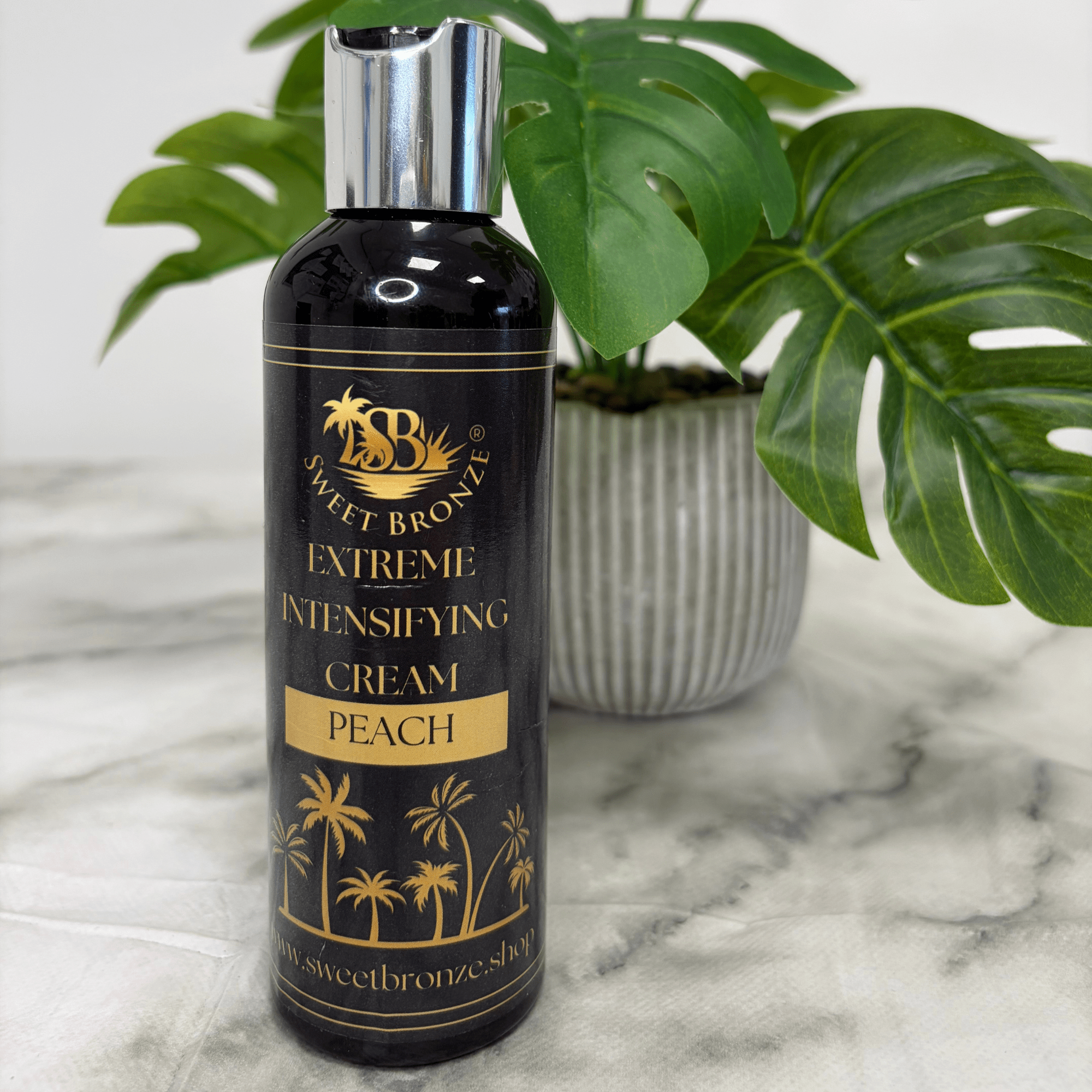 Bottle of Sweet Bronz Extreme Intensifying Cream Peach on a marble surface with a plant in the background