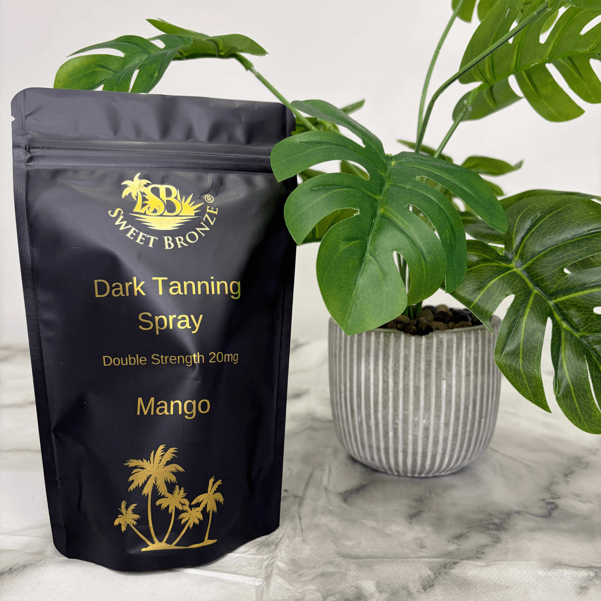 Black packaging of Sweet Bronze Dark Tanning Spray with gold text and plant in the background
